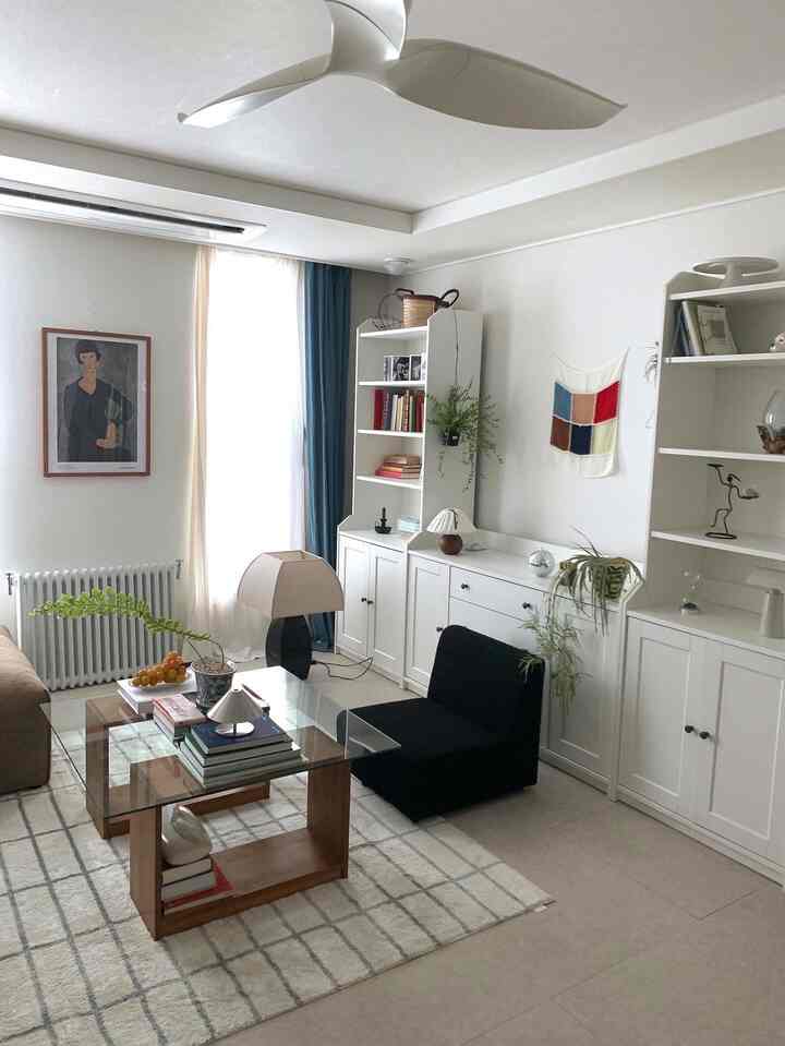 白とナチュラルカラーのリビング、黒いソファとガラスのコーヒーテーブル、本棚、ラグが配置された落ち着いた雰囲気のインテリア