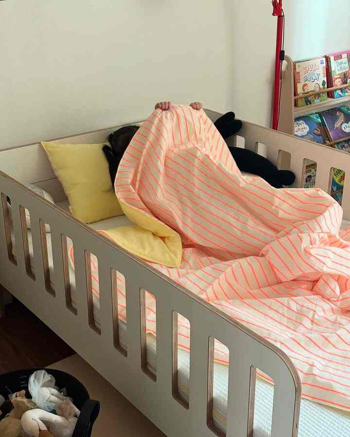 柔らかな黄色とピンクの色調の子供部屋、ベビーベッドと整理されたおもちゃが印象的な暖かい空間