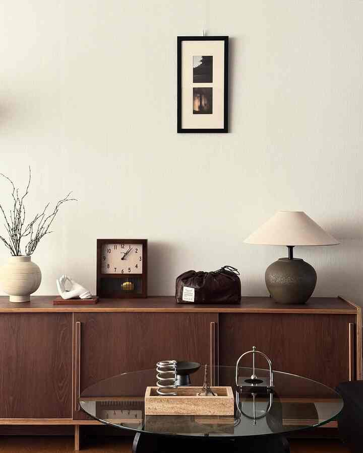 温かみのある木目調家具と黒い額縁、テーブルランプが調和した落ち着いたモダンなリビング空間
