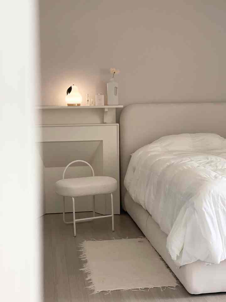 ホワイトとベージュのトーンの寝室、ベッドとスツール、ワイヤレスランプが配置された温かみのあるナチュラルモダンな空間