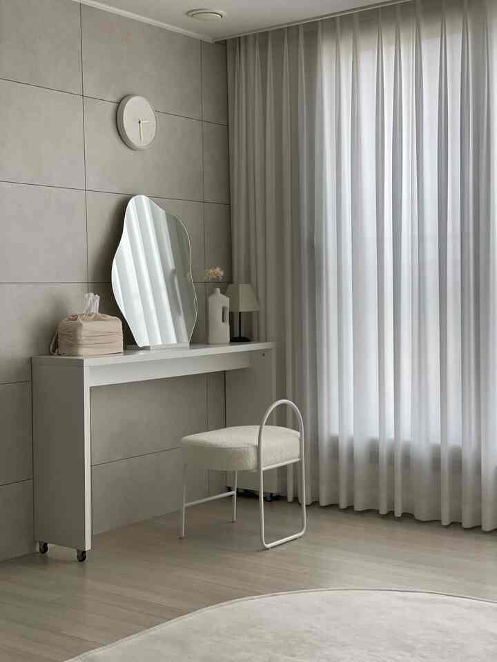 A white and gray toned living space featuring a sleek vanity and stool with a simple, hotel-like modern interior