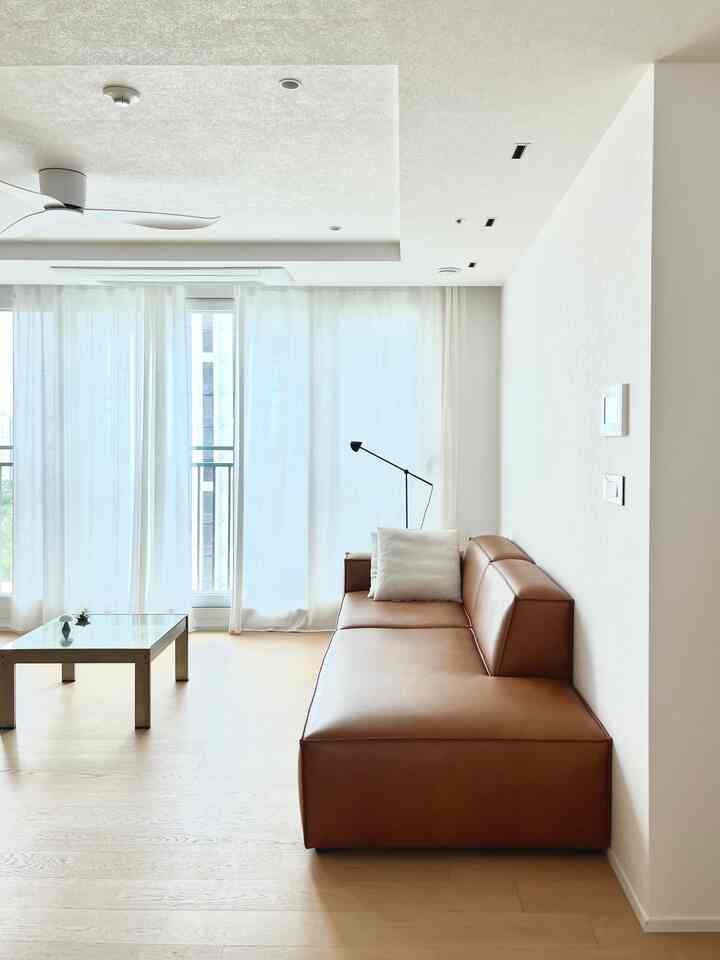 明るいホワイトトーンのリビングルーム、ブラウンレザーのソファとコーヒーテーブルが配置されたモダンでナチュラルなインテリア