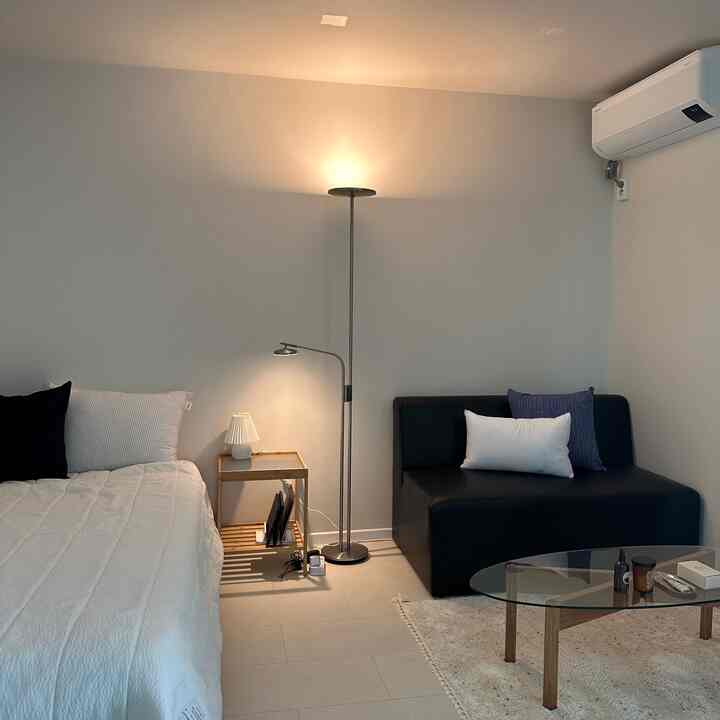 モノトーンでミニマルな小さなリビング兼寝室、セミシングルベッドとコンパクトなソファを配置した空間