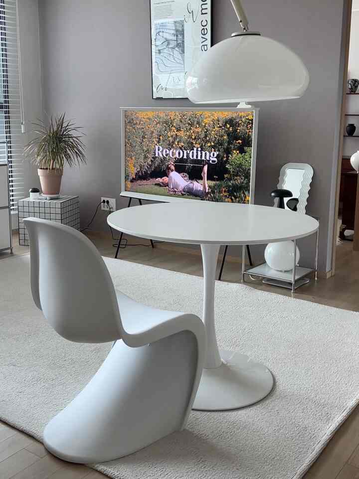 Bright white and light brown toned living room featuring a round dining table, chair, TV stand, and floor lamp in a minimal setting