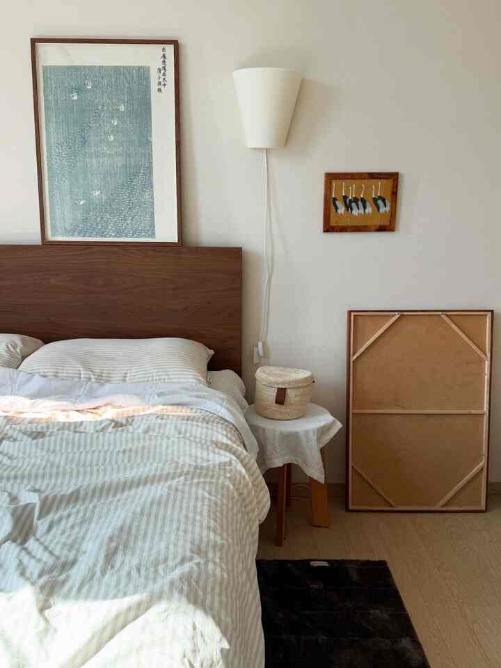 ナチュラルな木目調とホワイトが調和した寝室、木製ベッドフレームと額縁が配置された温かみのある雰囲気のインテリア