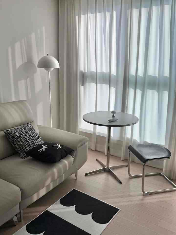 Modern and simple living room in white, silver, and black tones featuring a sofa, round table, and stool