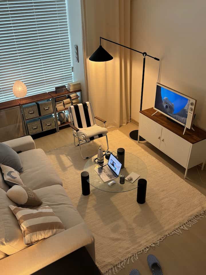 白と黒のトーンが調和するワンルームのリビング、モダンなフロアランプとガラスのコーヒーテーブルが配置されたすっきりとした空間