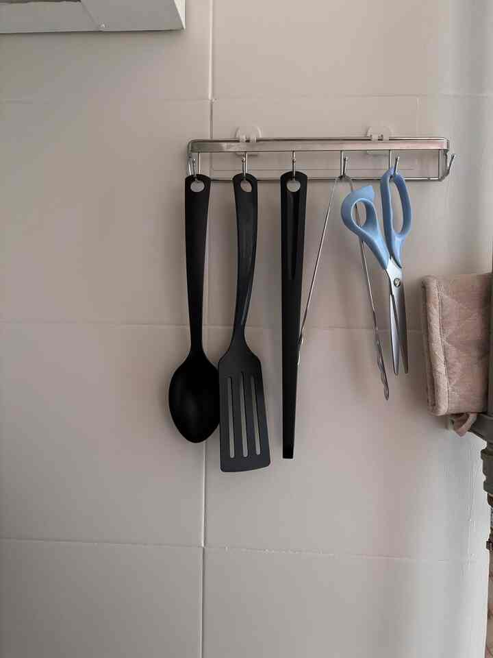 ベージュ色調のキッチン壁にシルバーの調理器具ラックがあり、黒と青の調理器具が掛けられたすっきりとした空間