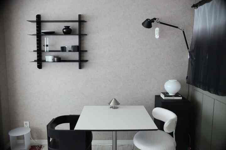 白と黒のトーンの小さなリビング、シンプルなテーブルと二脚の椅子、壁棚と壁灯が配置されたモダンな雰囲気のあるインテリア