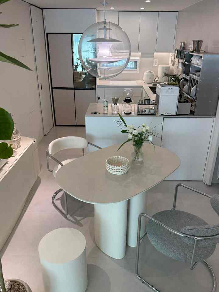 白とグレーのトーンのキッチン空間、中央にベージュのダイニングテーブルと椅子が配置されたミニマルな雰囲気のホームカフェインテリア