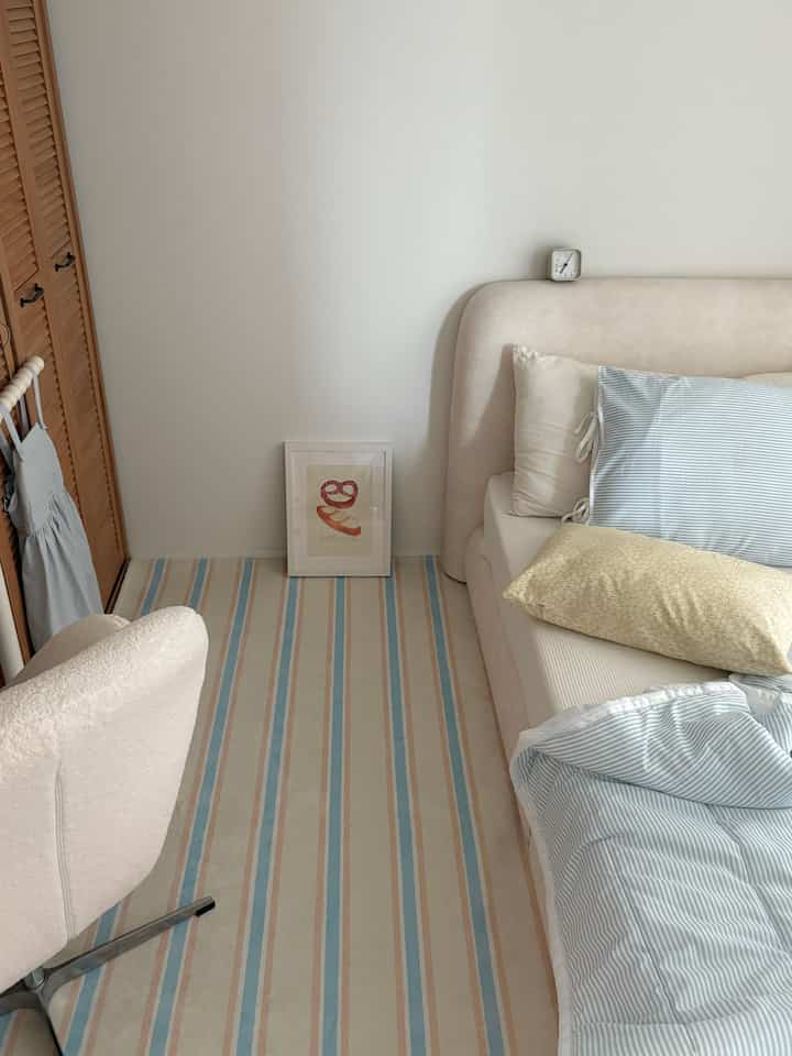 ベージュとスカイブルーの色調の子供部屋、寝具付きのベッドとラグ、額縁が配置された落ち着いた印象的な空間
