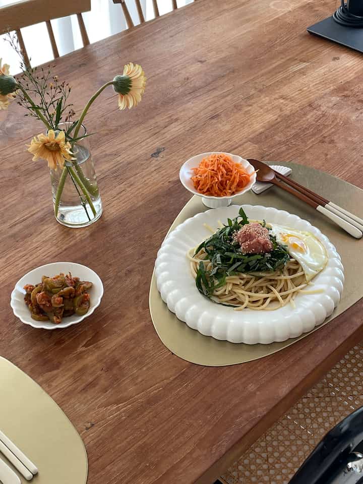 温かみのある木目調のダイニング、花瓶と明太子パスタが置かれたシンプルでナチュラルな空間