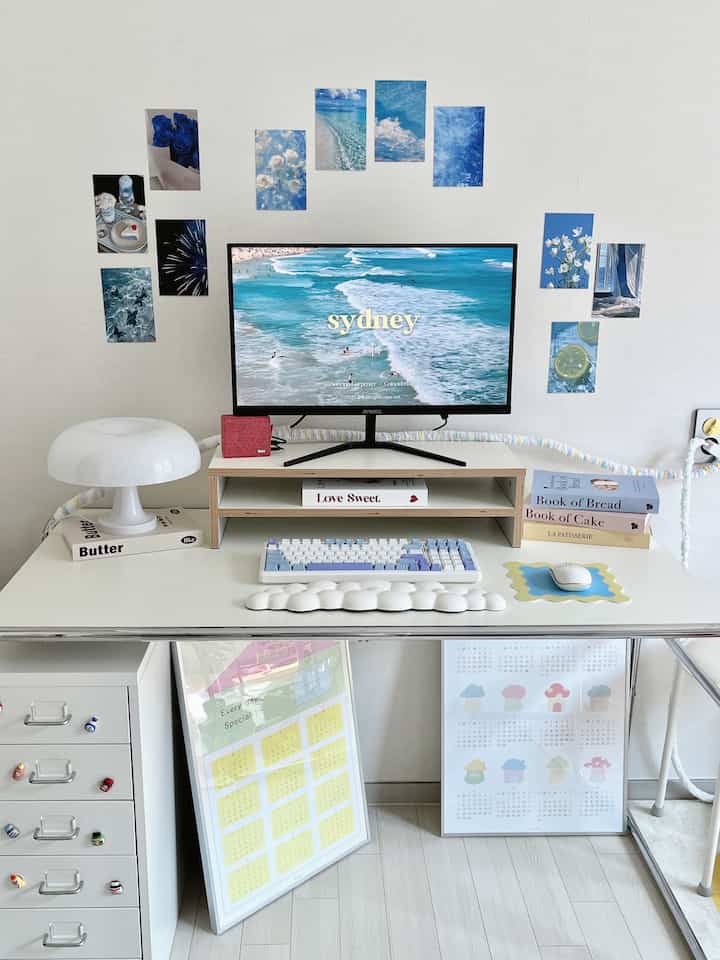 Bright white and sky blue studio workspace with a desk featuring a computer and blue-themed postcards on the wall