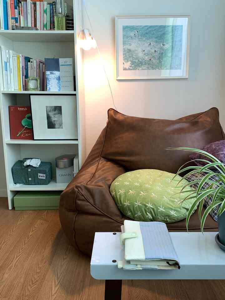 Natural tone living room featuring brown leather bean bag, white bookshelf, and string lights creating cozy atmosphere