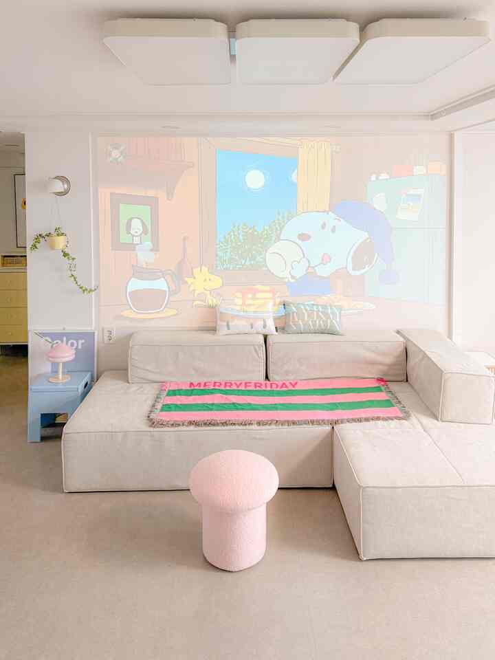 Pastel-toned living room with soft beige sofa and pink mushroom-shaped bouclé stool, featuring a cozy atmosphere with cartoon projection on the wall