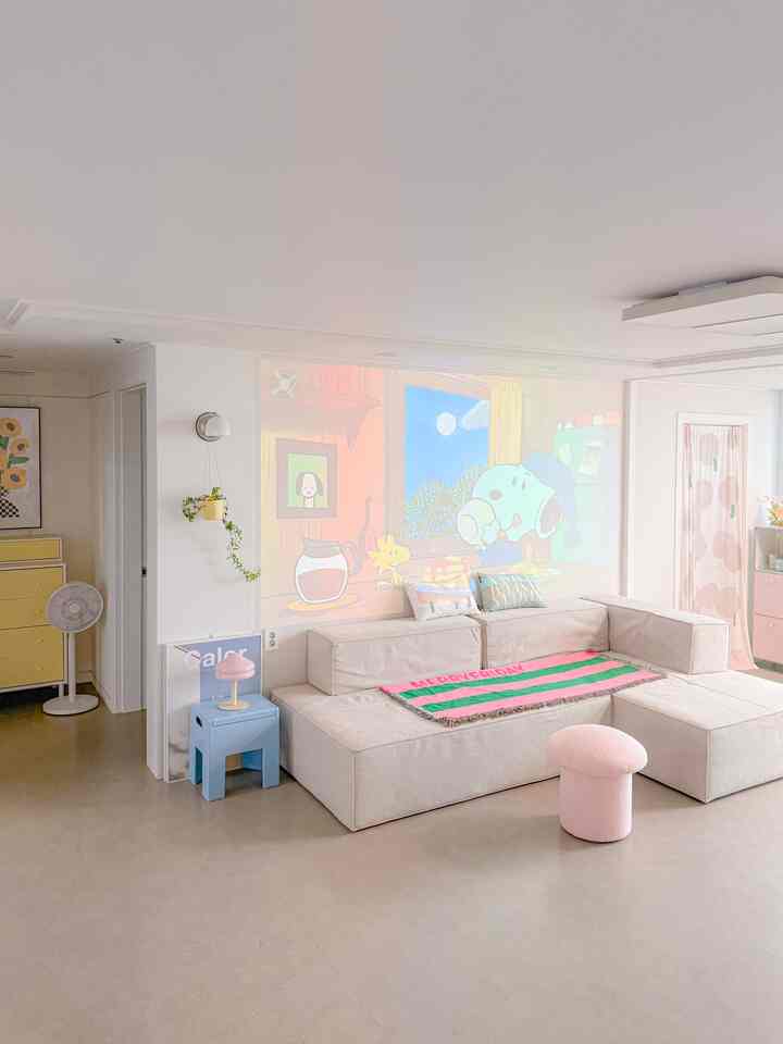 A bright living room in white and beige tones, featuring a beige sofa and a small pink stool creating a cozy atmosphere