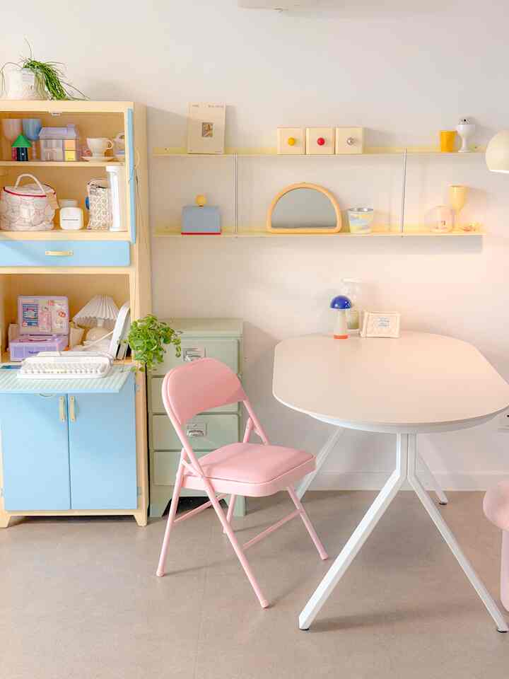 Compact workspace featuring white and pastel furniture, with a pink folding chair and multi-use storage cabinet creating a cozy atmosphere