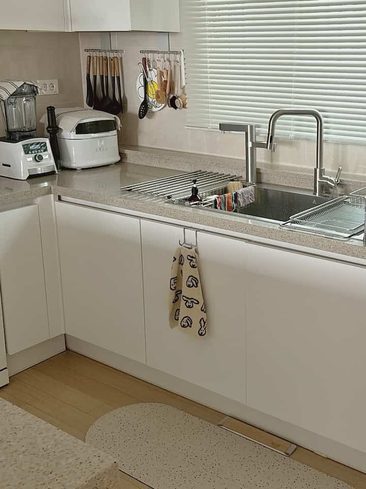 明るい白を基調としたモダンなキッチン、ステンレス製のシンクと調理器具が整然と配置された印象的な空間