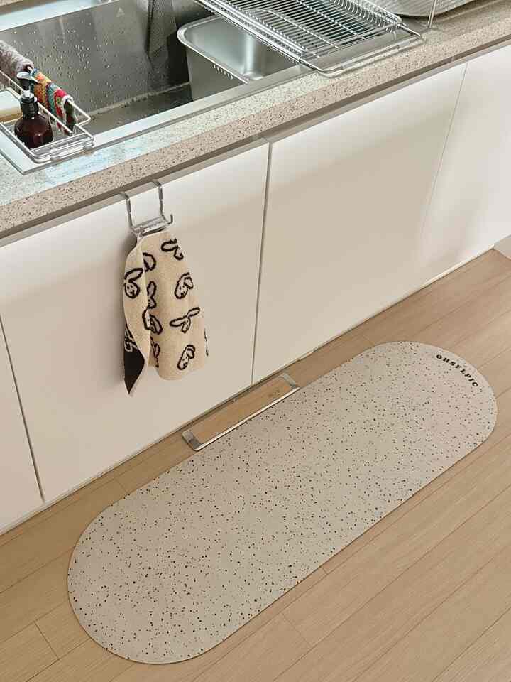 白いキッチンシンク前にベージュの珪藻土バスマットと柄のキッチンタオルが掛けられた清潔感のある空間