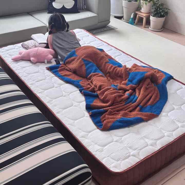 白と茶色のトーンの寝室、中央にベッドとブランケットが配置され、子供が横たわる印象的な空間