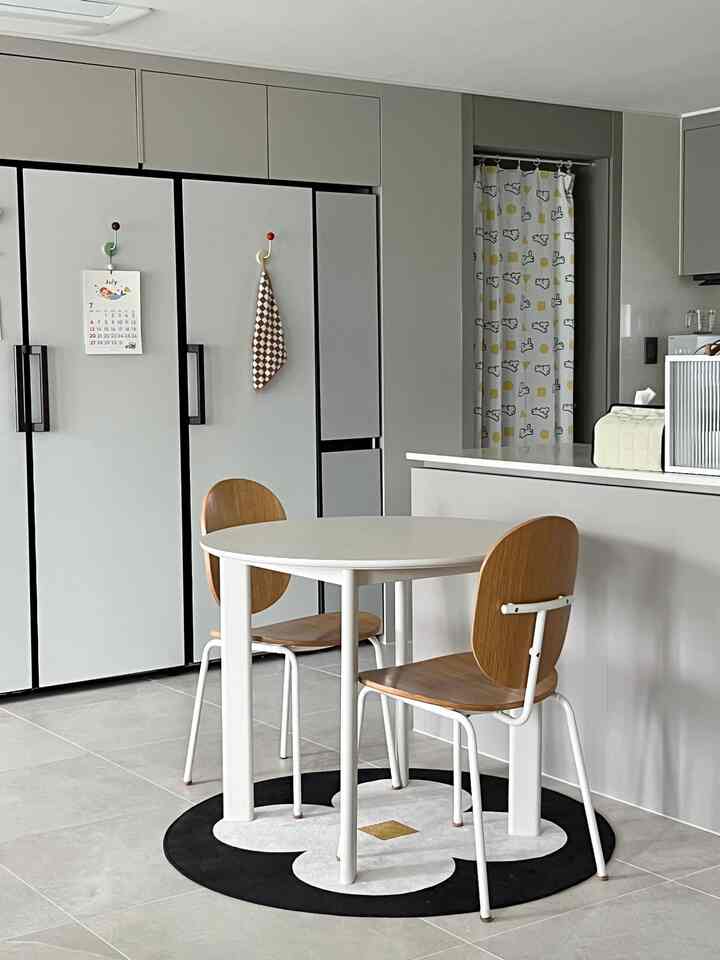 白とグレーの色調のキッチンスペース、丸いダイニングテーブルと木製チェアが整然と配置されたモダンな雰囲気