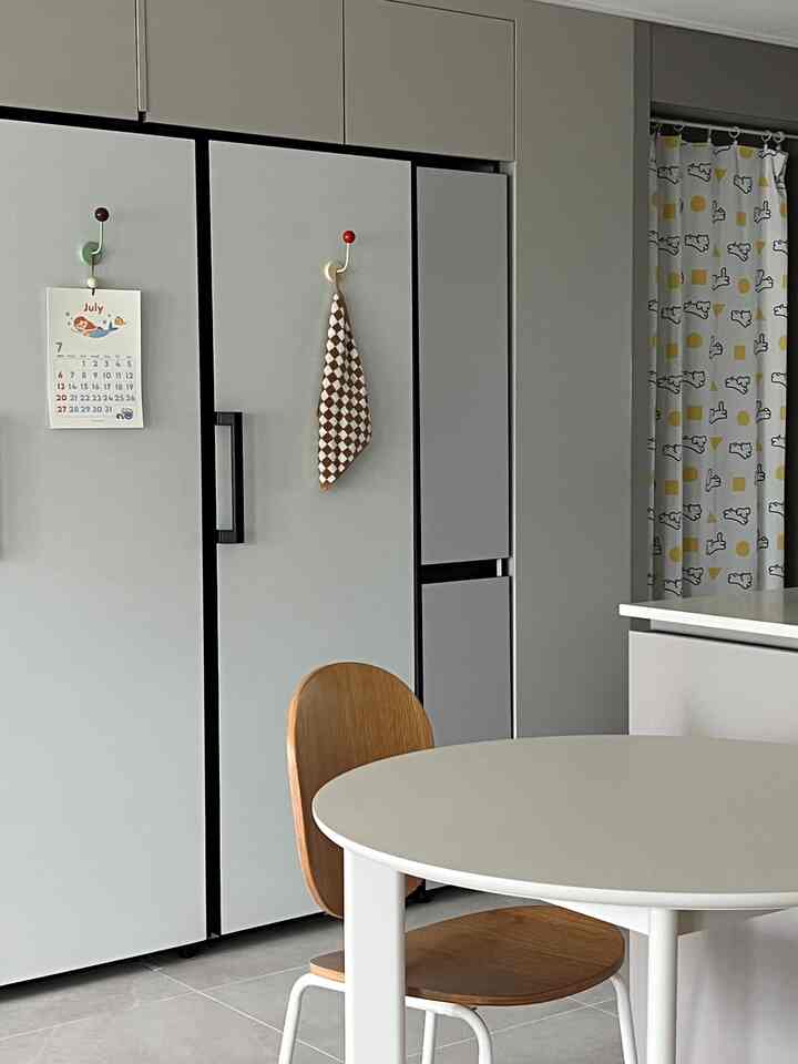 グレーと白のトーンのモダンなキッチン空間、丸いダイニングテーブルと木製チェア、かわいい柄のカーテンが配置されたインテリア