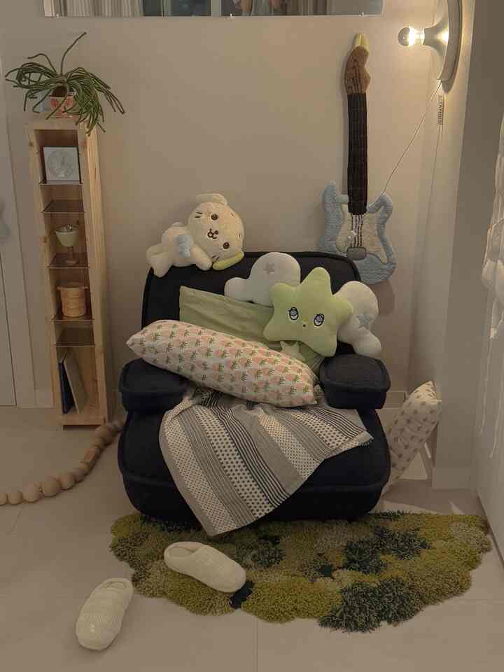 落ち着いたナチュラルカラーの狭い寝室に、中央に配置されたダークブルーのアームチェアとグリーンのラグが温かみのある雰囲気を醸し出している。