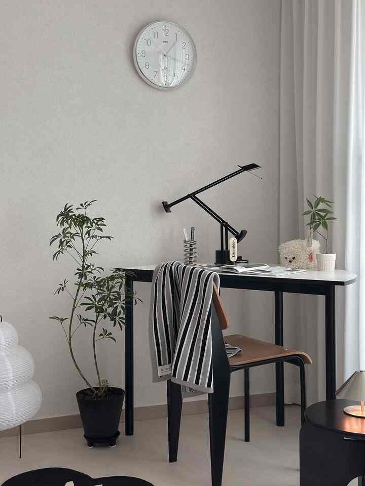 白い壁と黒い家具が調和したシンプルモダンなホームオフィス、デスクランプと植物が配置された落ち着いた作業空間