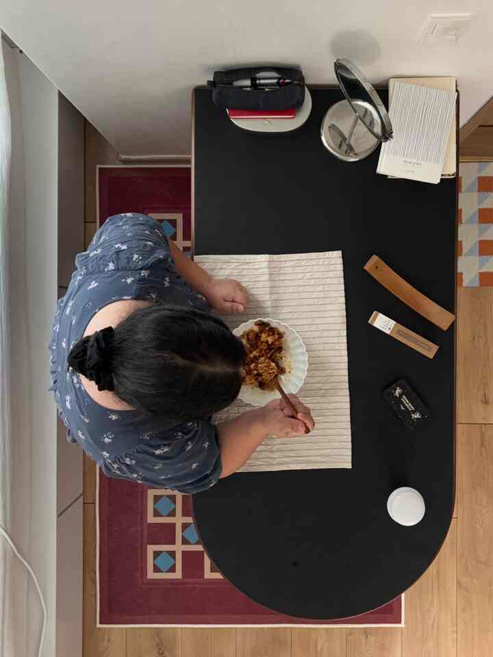 木目調の床と黒いダイニングテーブルがあるリビング、テーブルクロスの上で食事をしている一人の人物がいる落ち着いた空間