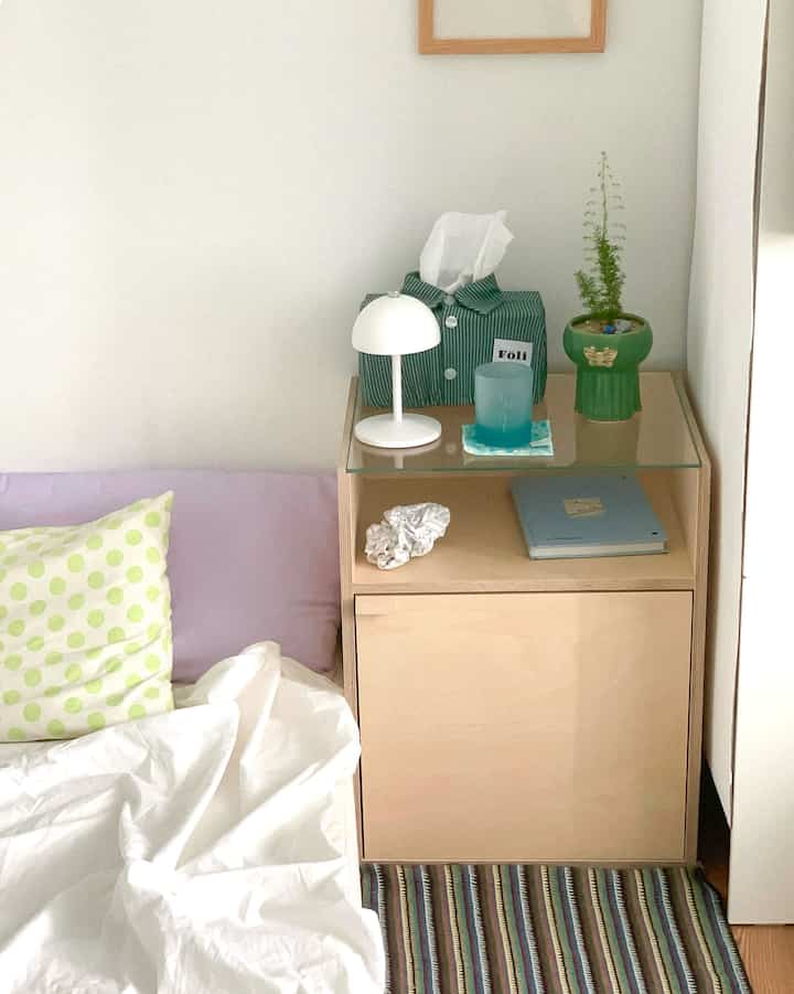 White and natural tone bedroom featuring a side table with a potted plant, creating a cozy atmosphere