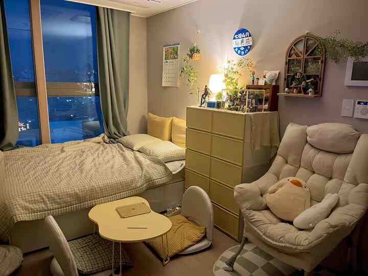 黄色とベージュのトーンのワンルーム寝室、黄色のチェストとベッド、快適なソファとテーブルランプが配置された雰囲気のあるインテリア