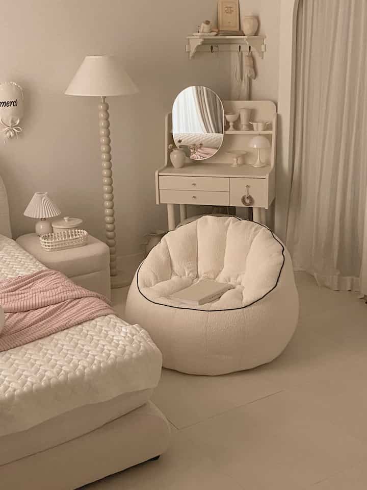 ベージュトーンの寝室空間、大きなビーズクッションとベッド、化粧台が配置された落ち着いたシンプルなインテリア
