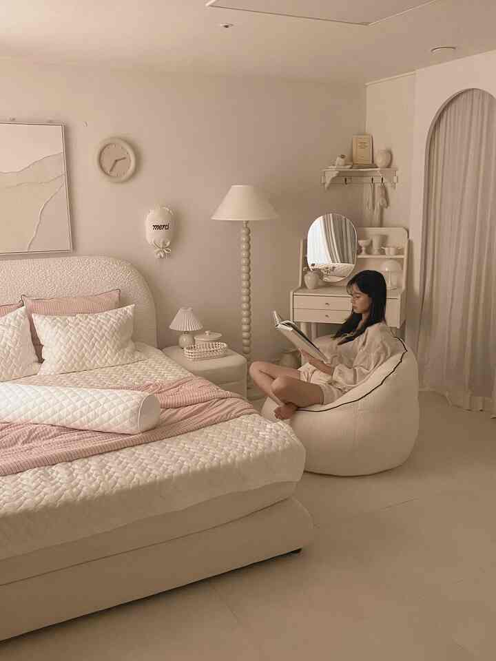 アイボリーとベージュのトーンの寝室、白いベッドとビーズクッションが配置された雰囲気のある読書空間