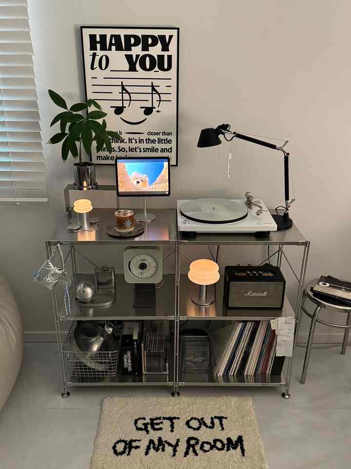 Silver-toned music zone featuring MUJI stainless steel shelves, Denon turntable, lighting, and poster in a modern interior