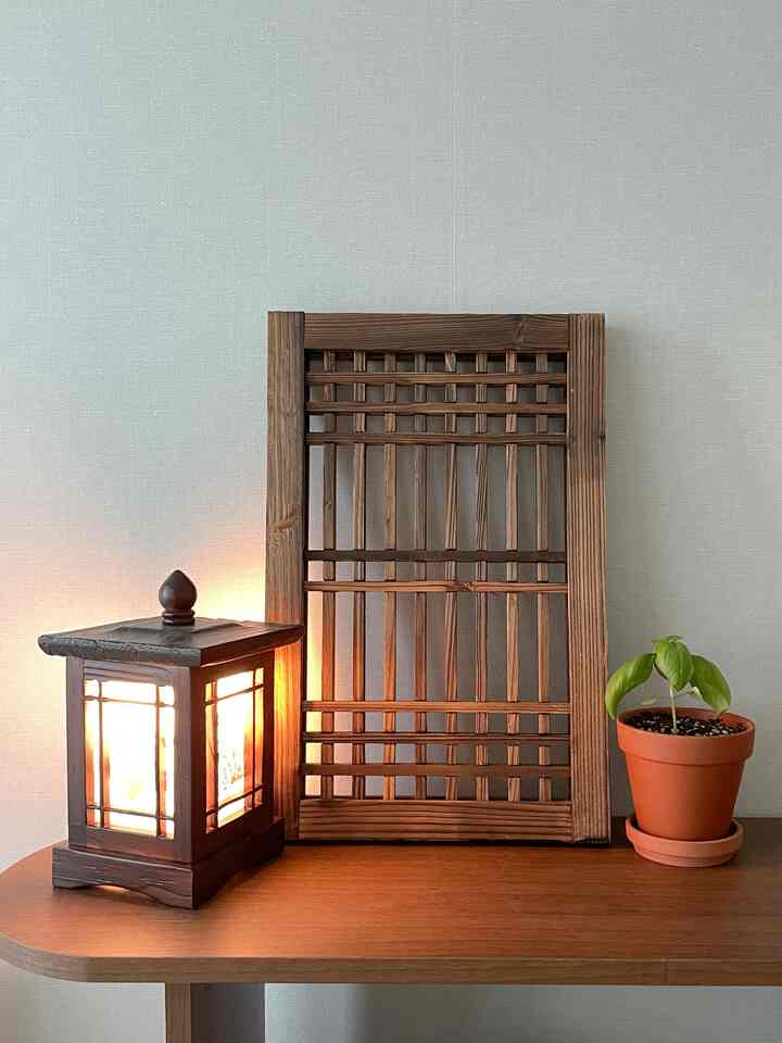 茶色の木製テーブルの上に伝統的な韓国風の格子戸とランプ、小さな観葉植物が配置された自然な雰囲気のオブジェ空間