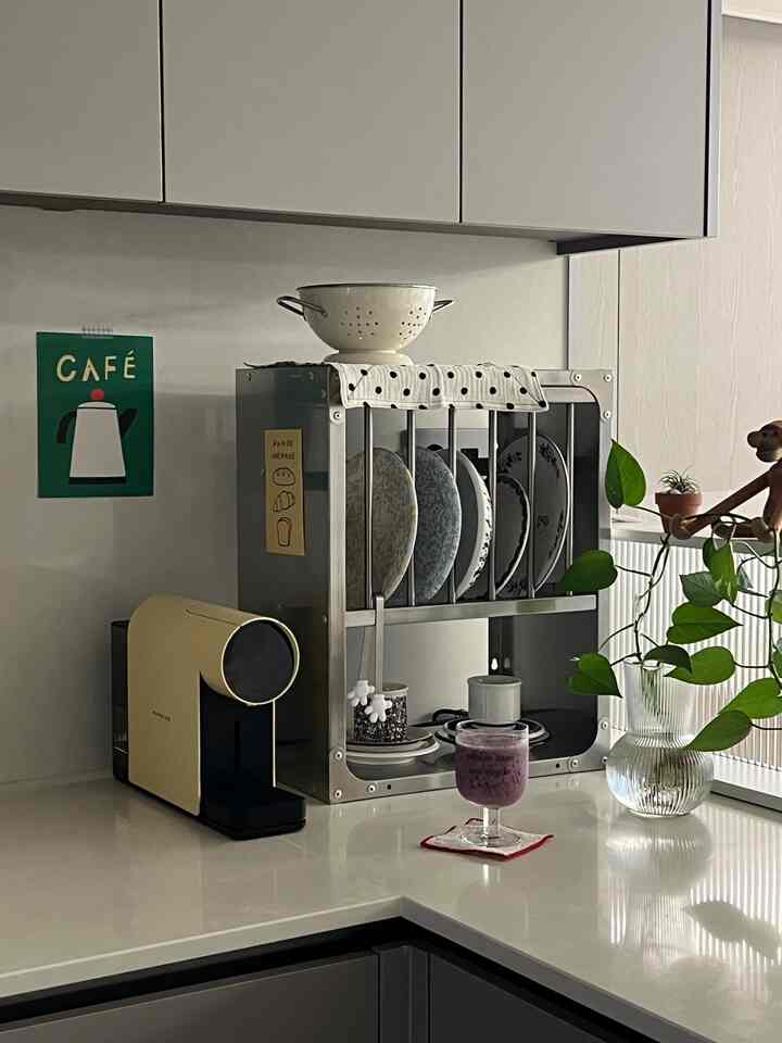 白とスチールの色調のキッチン空間で、カプセルマシンと食器ラックが配置されたモダンなおうちカフェの雰囲気のあるインテリア