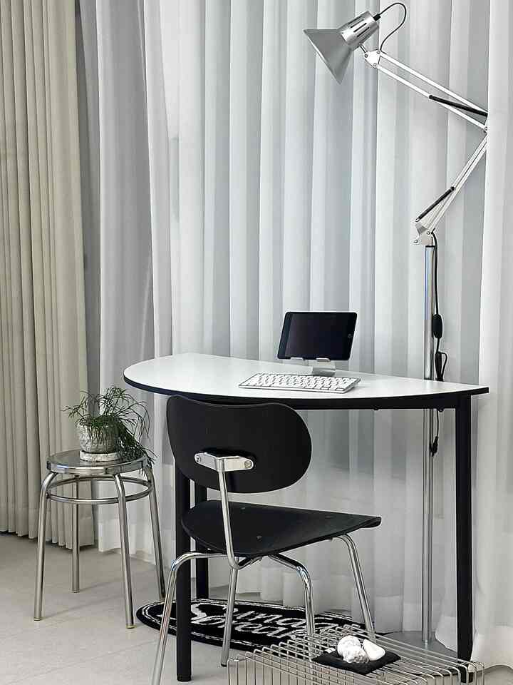 A modern home office in white and black tones featuring a desk, chair, stool, and floor lamp arranged neatly
