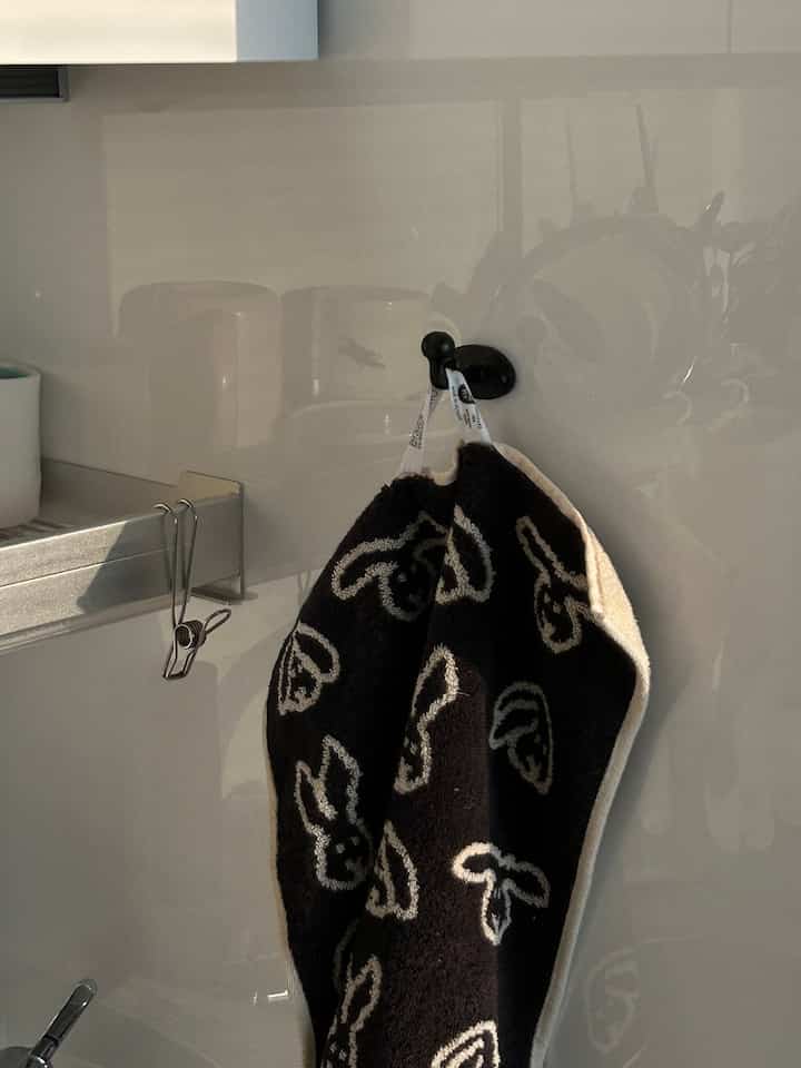 白い壁とスチール棚があるキッチンの壁に黒いウサギ柄のタオルが掛かっている様子