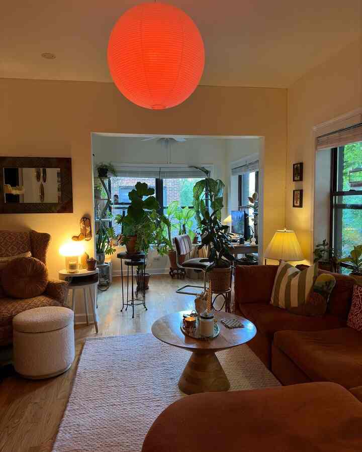 Warm orange pendant light and brown sofa in a natural modern living room featuring various green plants and cozy lighting