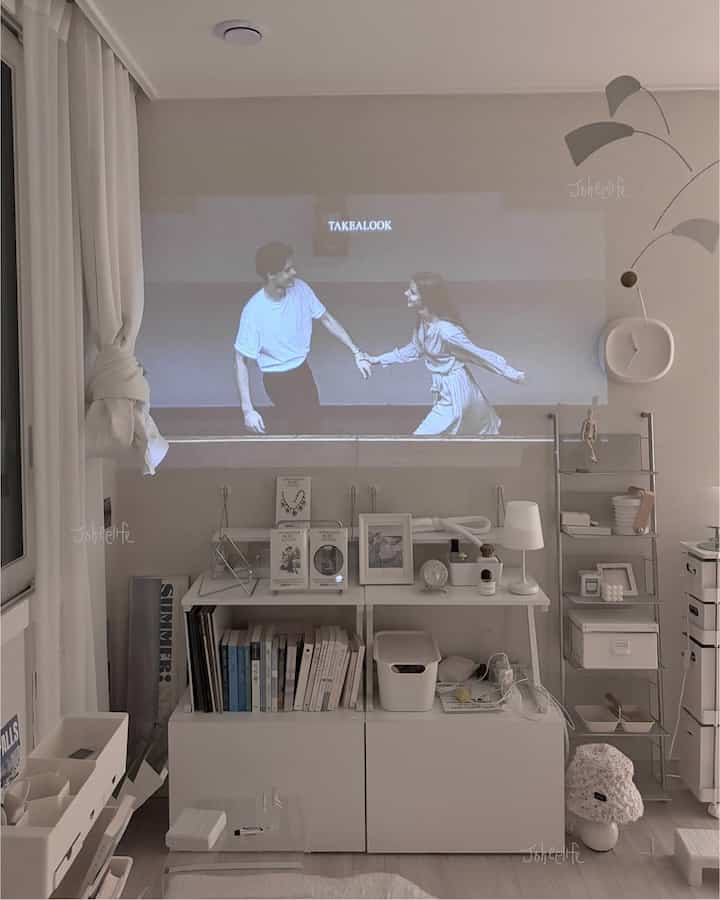 白を基調としたミッドセンチュリーモダンの寝室、モジュラー棚と鉄製はしご棚が整った収納スペースと壁のプロジェクター映像