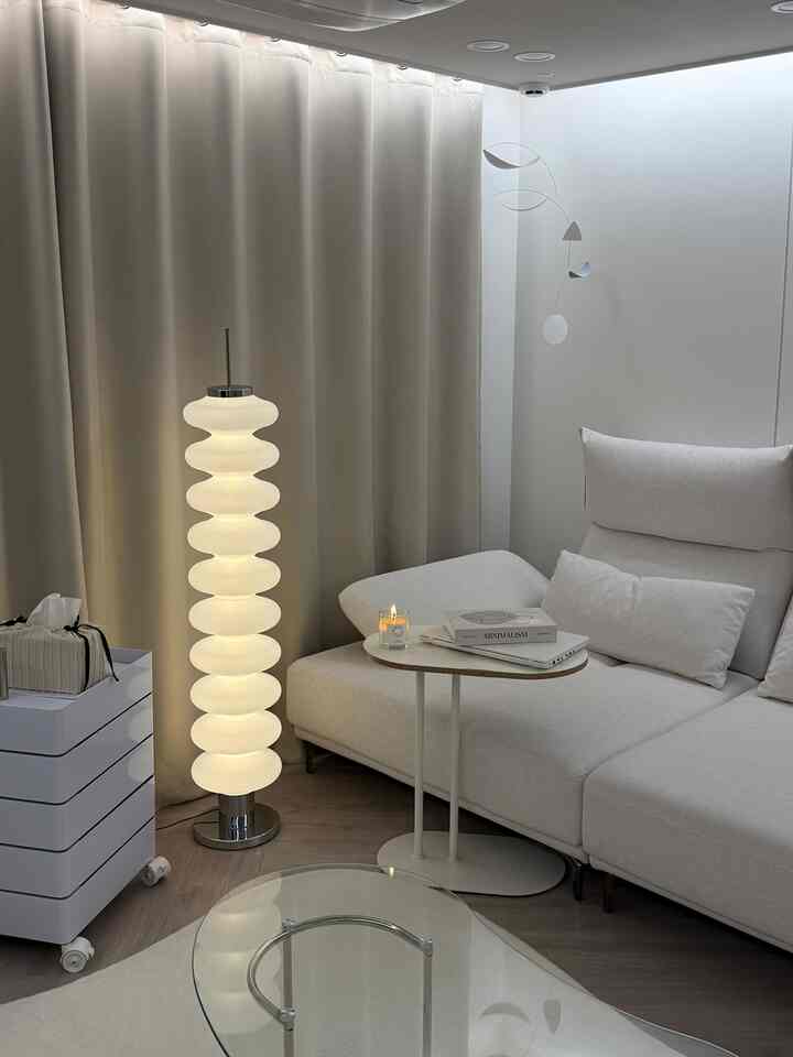 明るいホワイトとベージュのトーンのリビング、ファブリックソファとサイドテーブル、個性的なフロアランプとモビールが配置されたモダンでナチュラルな空間