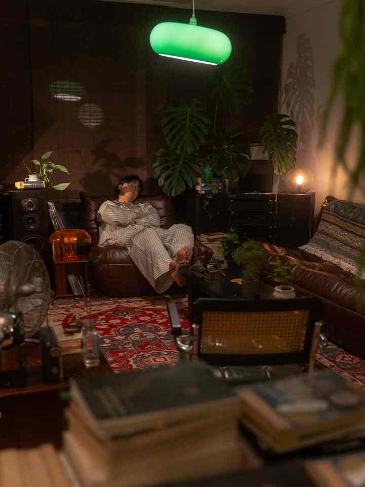 温かみのあるブラウンとグリーンのトーンのリビング、ヴィンテージ家具とムードライトが配置された雰囲気のある空間