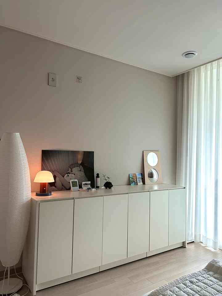 白とナチュラルカラーの落ち着いた寝室、中央に鉄製収納棚と照明、トレイ、鏡などの小物が配置された雰囲気のあるインテリア