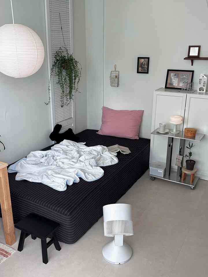 白と黒の対比によるシンプルなワンルーム寝室、無線扇風機と冷感布団が配置された居心地のよい空間