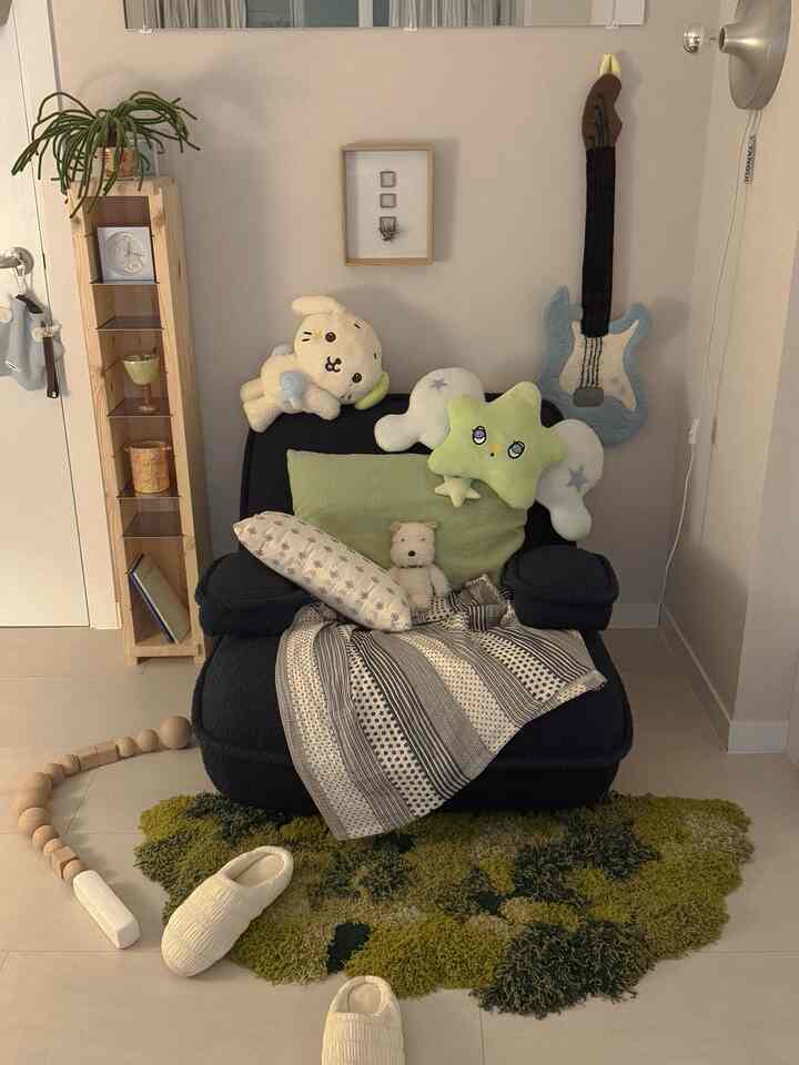 ナチュラルな色調のワンルームリビング、黒の1人掛けアームチェアソファとグリーンラグが配置された居心地の良いコンパクトな空間