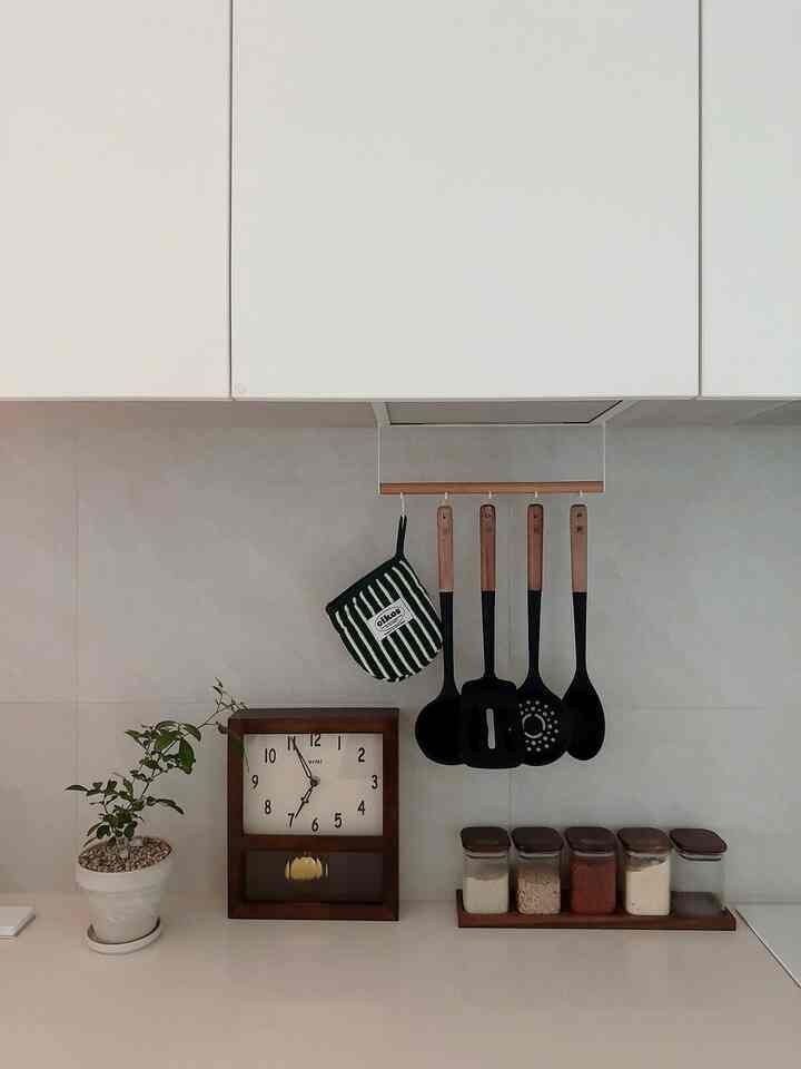 A white and wood-toned kitchen featuring a retro clock, kitchen utensils, and a green plant creating a cozy atmosphere