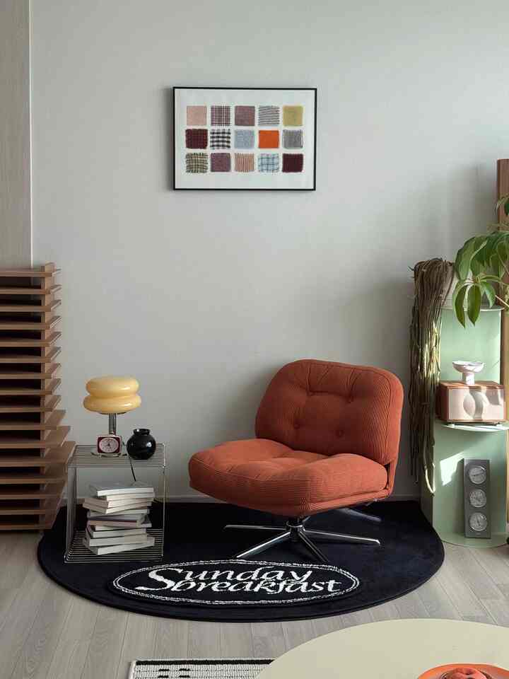 Natural-toned living room space featuring an orange fabric armchair, black rug, picture frame, and plants creating a cozy atmosphere