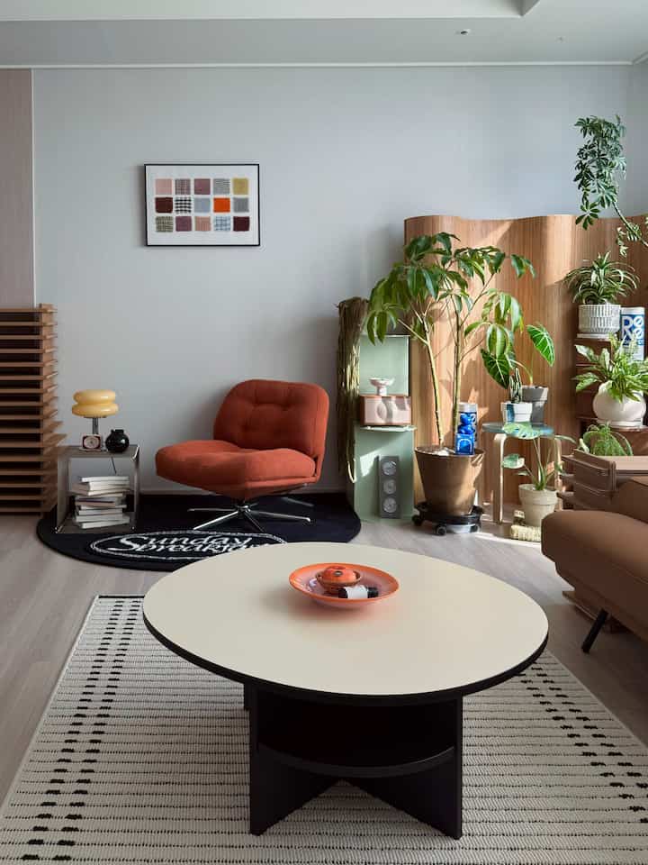 Natural tone living room featuring orange armchair, coffee table, and various plants with simple modern interior