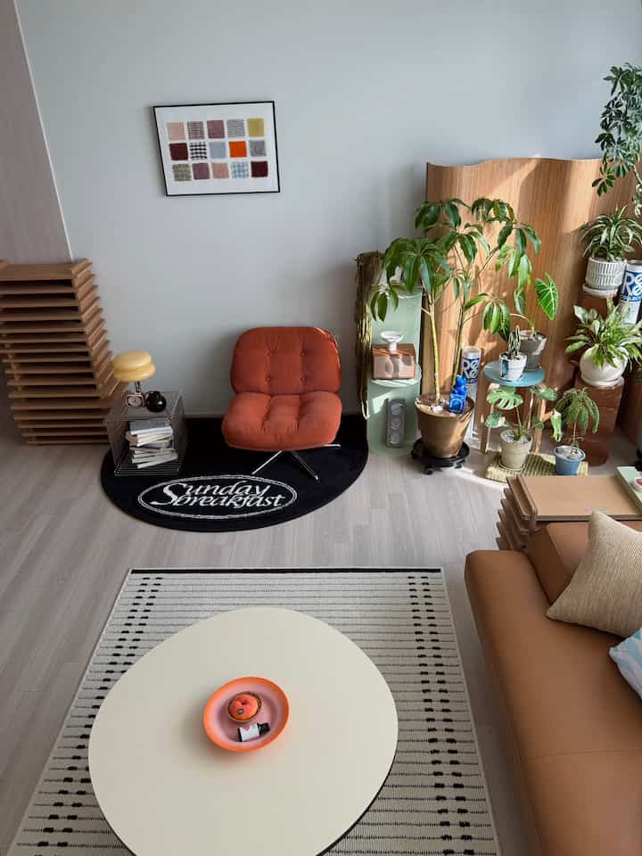Natural-toned living room featuring orange stool, leather sofa, and various plants in a modern, simple space