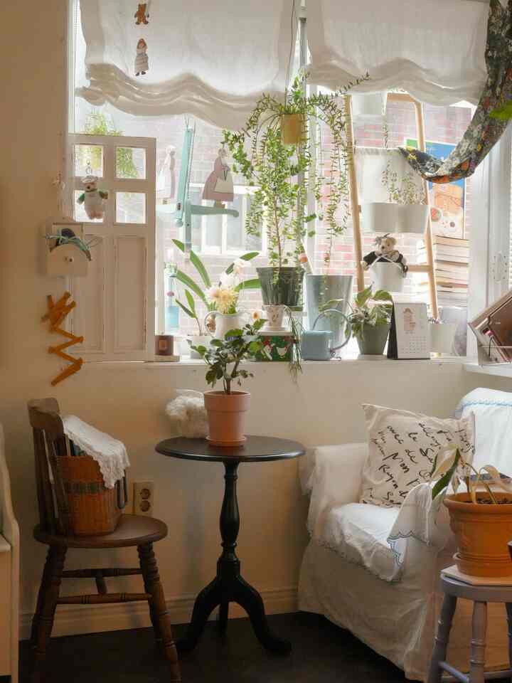 白とベージュのトーンが漂うバルコニーのあるヴィンテージ風リビング、植物とヴィンテージ家具が落ち着いた雰囲気を演出する